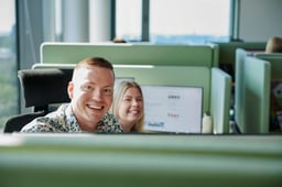 To personer i kontorlandskap ser i kamera og smiler