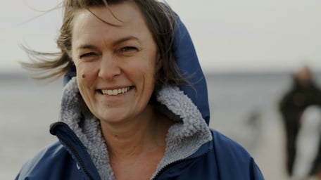 Smiling woman on windy beach looks into camera